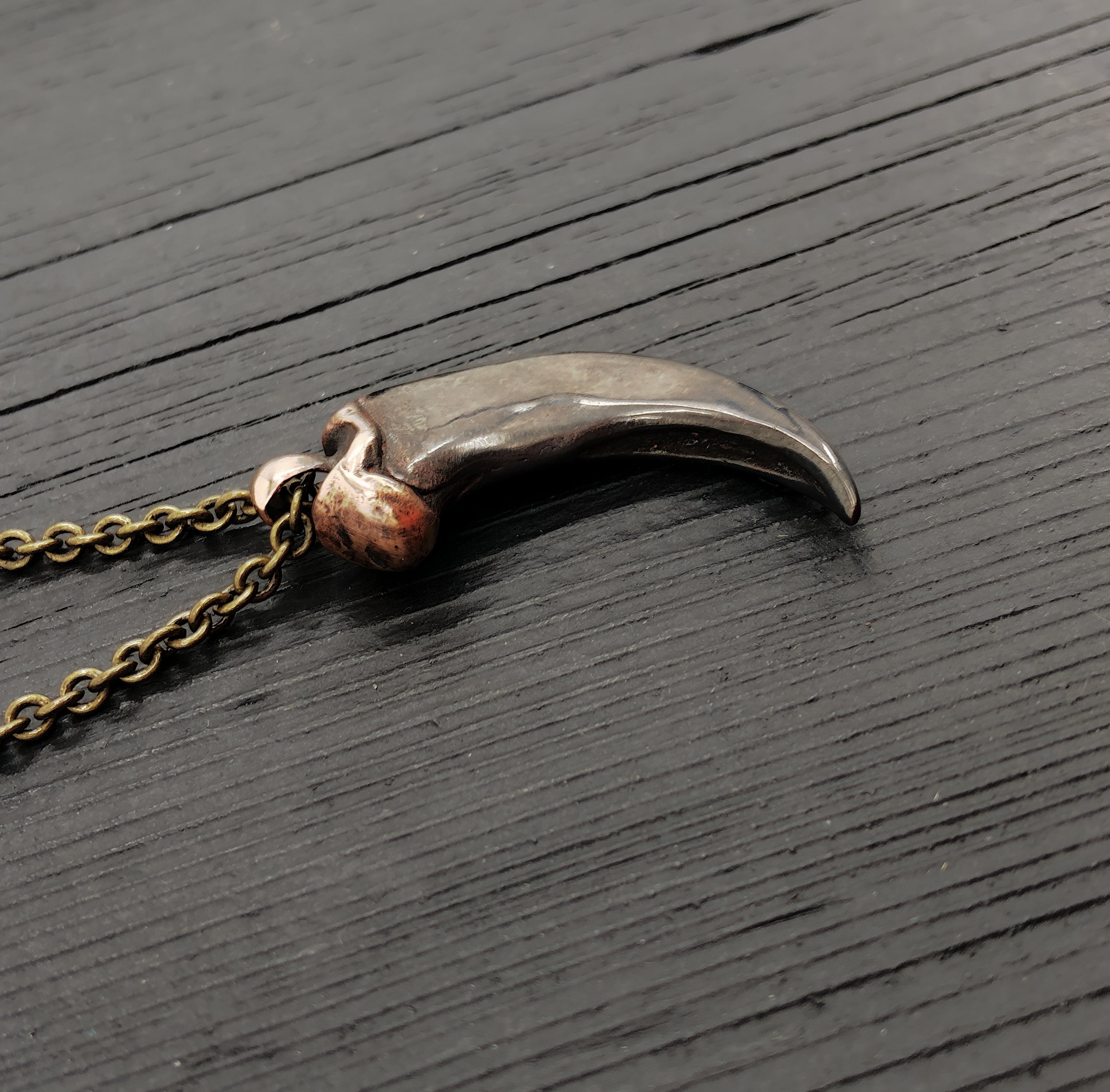 A bronze-colored canine tooth pendant necklace on a wooden surface.