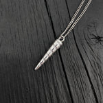 Silver cone-shaped pendant on a chain against a dark wooden background