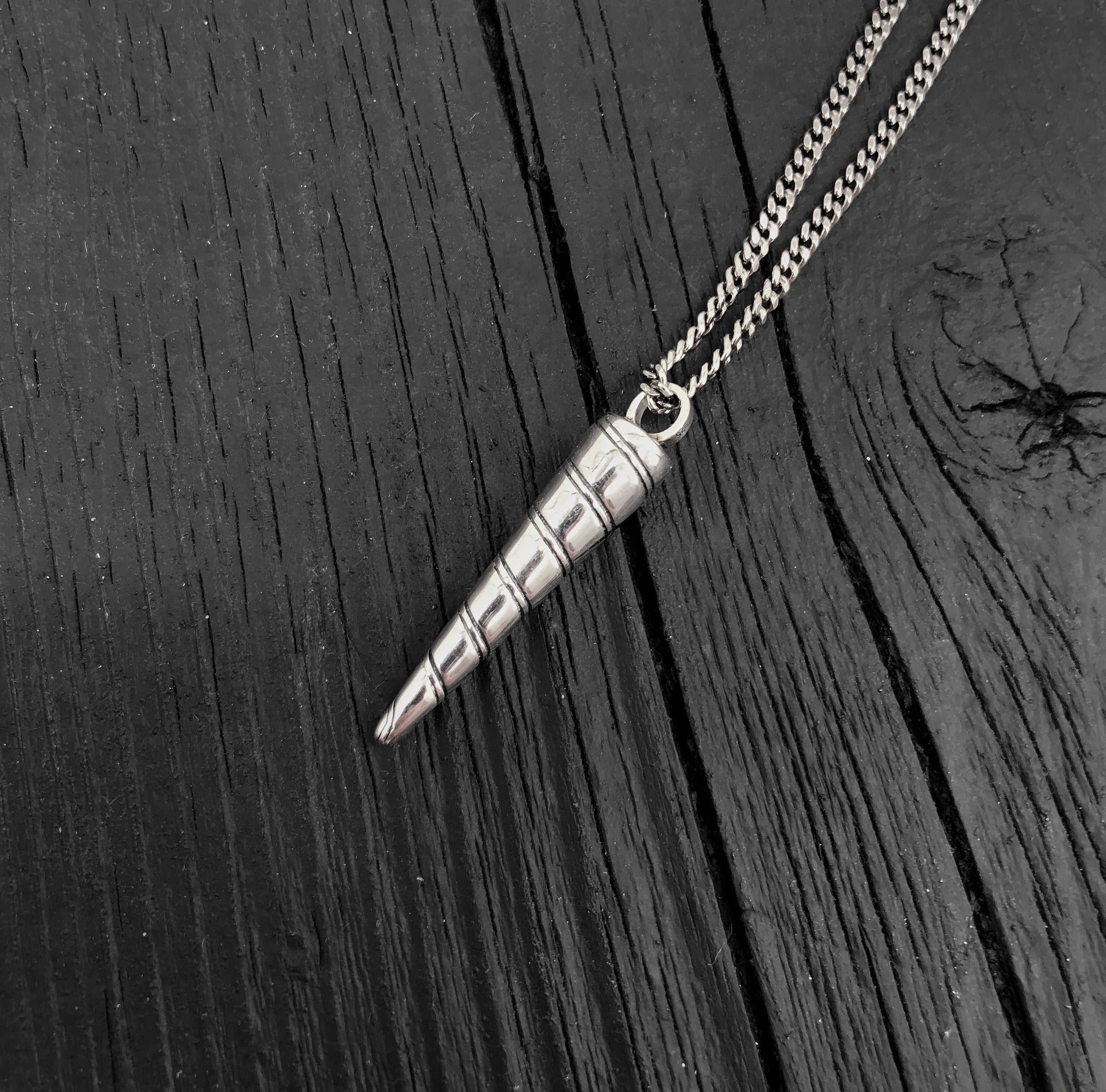 Silver cone-shaped pendant on a chain against a dark wooden background