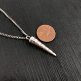 Silver spiral pendant necklace next to a penny on a dark wooden surface