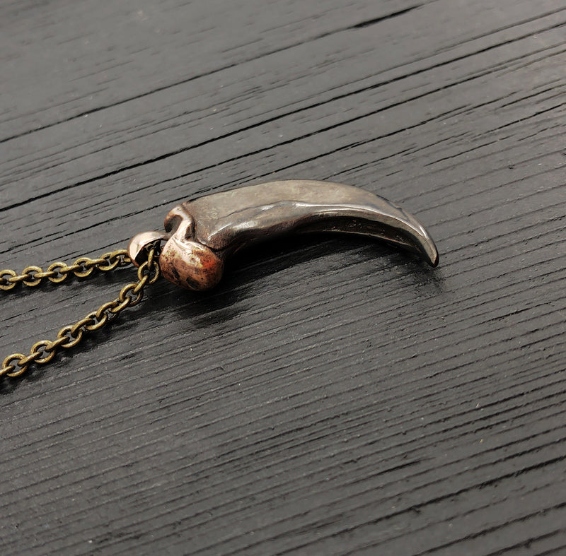 A bronze-colored canine tooth pendant necklace on a wooden surface.